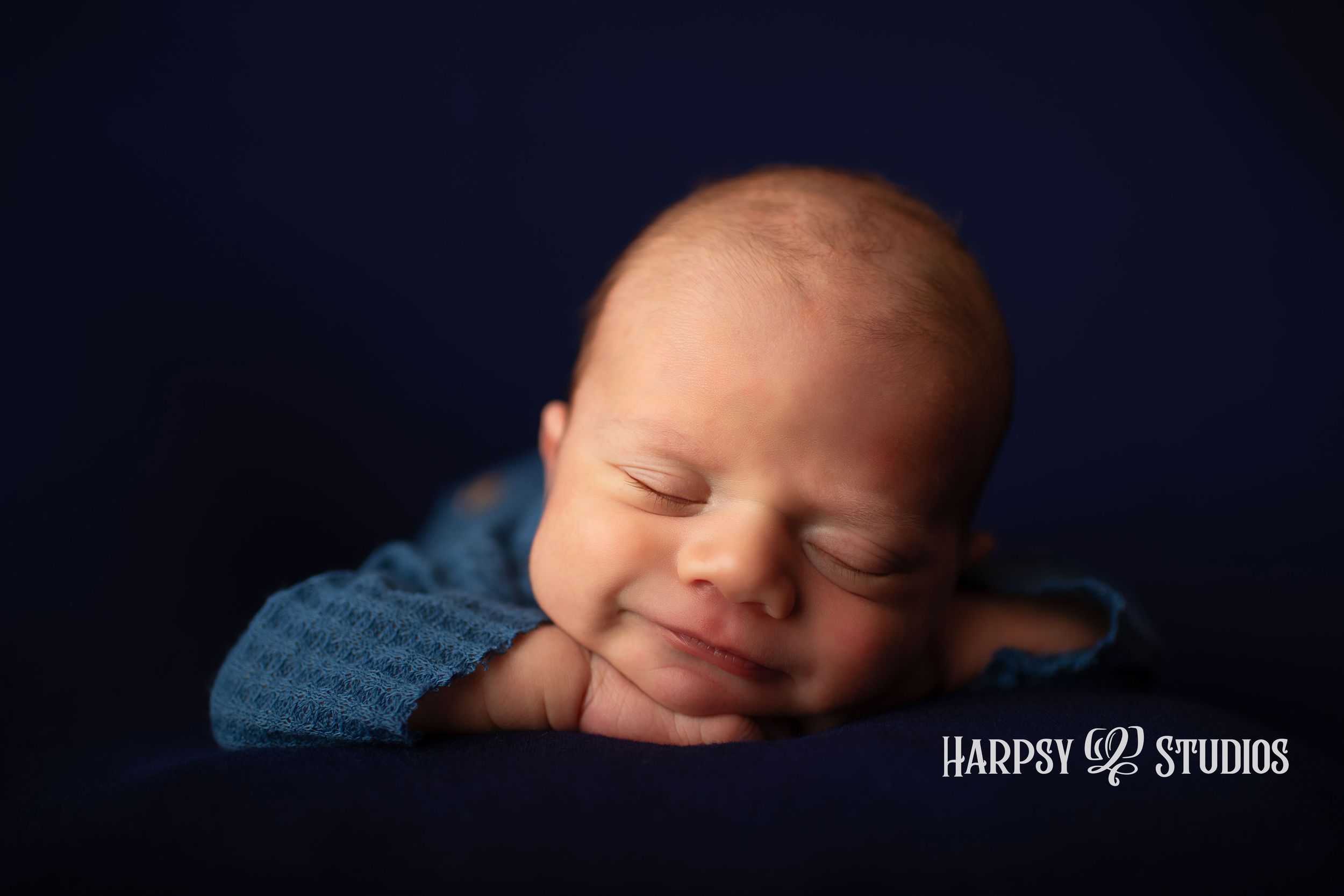 Smiling newborn photo; Lexington, SC best newborn photographer; newborn baby boy posed on blue with head on hands, smiling; newborn session
