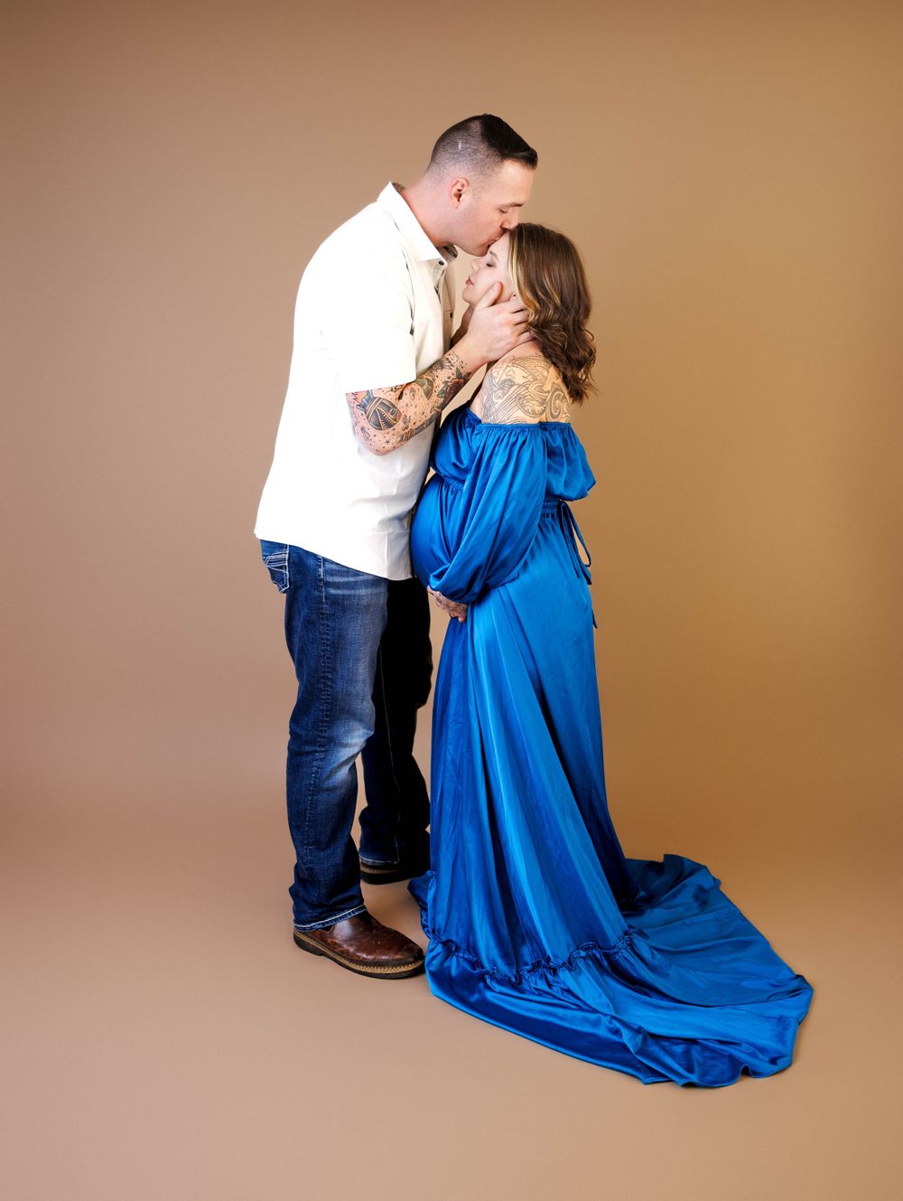 A couple embraces in a romantic pose against a brown backdrop, with the woman wearing a flowing royal blue gown.