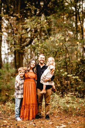 Family portrait in autumn forest with fallen leaves and natural lighting.