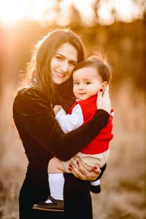 A tender moment between parent and baby in red sweater captured during golden hour sunset.