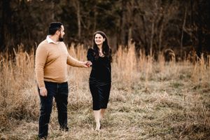 A romantic golden hour photoshoot in a field shows a couple walking together through tall grass at sunset.