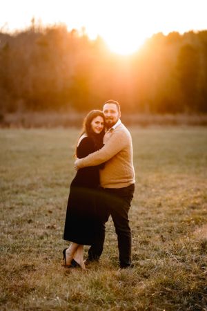 Couple embracing in golden sunset light in an open field.