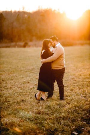 Romantic couple embracing in a field at sunset with warm golden light.
