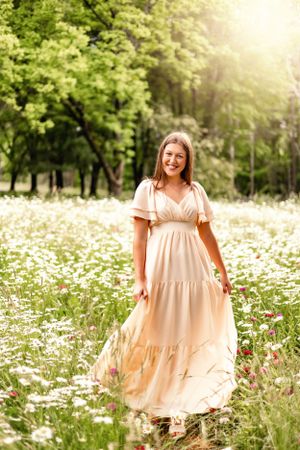 Ethereal summer scene with person in flowing maxi dress standing in field of white daisies and wildflowers.