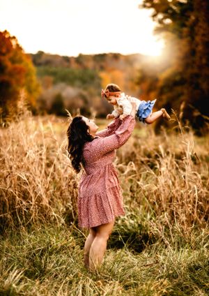 Parent lifting child in air during sunset in autumn field.