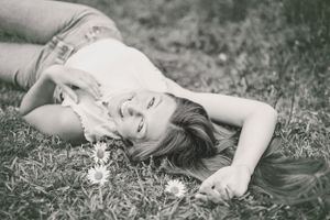 A dreamy black and white portrait of someone lying in grass with flowers.