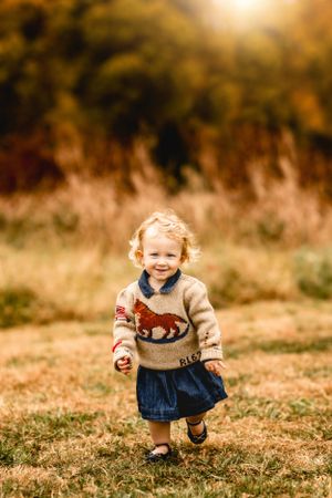 Young toddler in sweater running through autumn field at sunset.