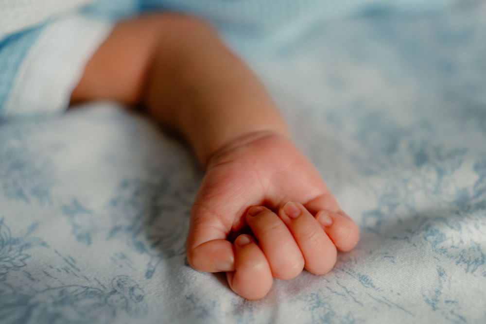 A tiny baby hand rests on soft blue and white floral bedding.