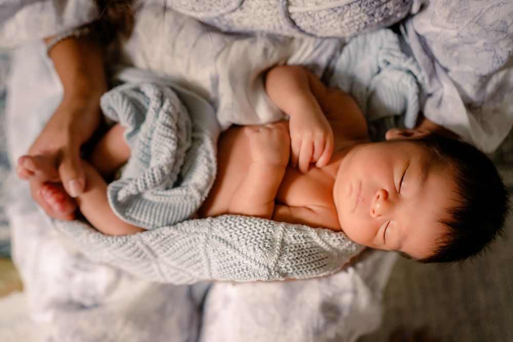 Peaceful sleeping newborn baby wrapped in soft gray knit blanket on white bedding.