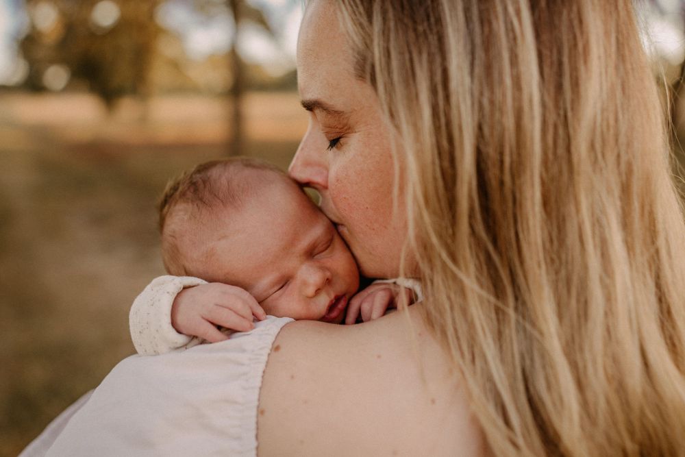 A tender moment as a parent kisses their sleeping newborn baby in warm sunlight.