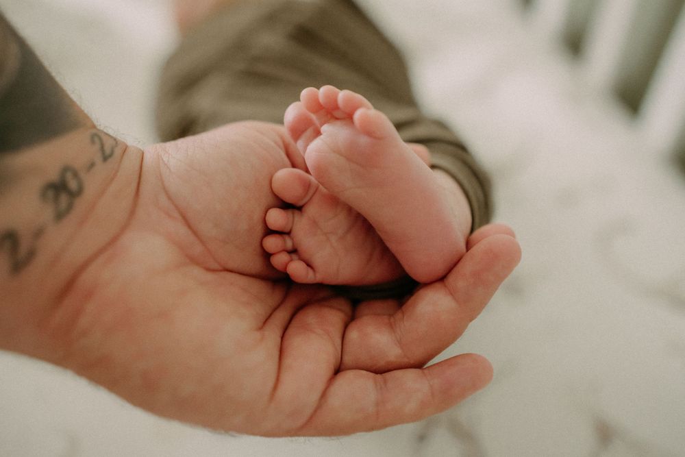 Close-up of tiny baby feet resting in tattooed hand.