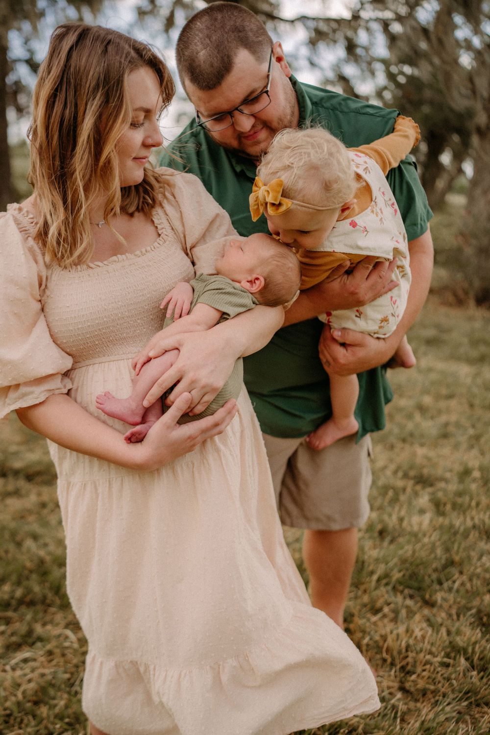 A tender family moment outdoors with parents holding infant twins in soft lighting and natural setting.