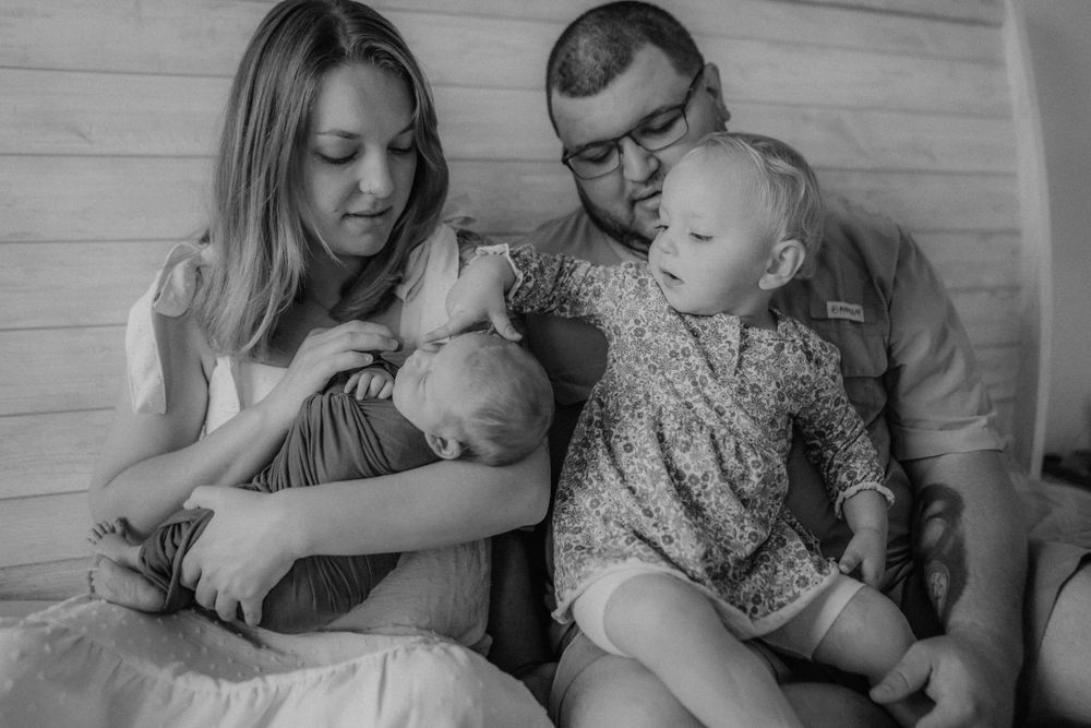 A tender black and white family photo shows parents with their two small children sitting together.