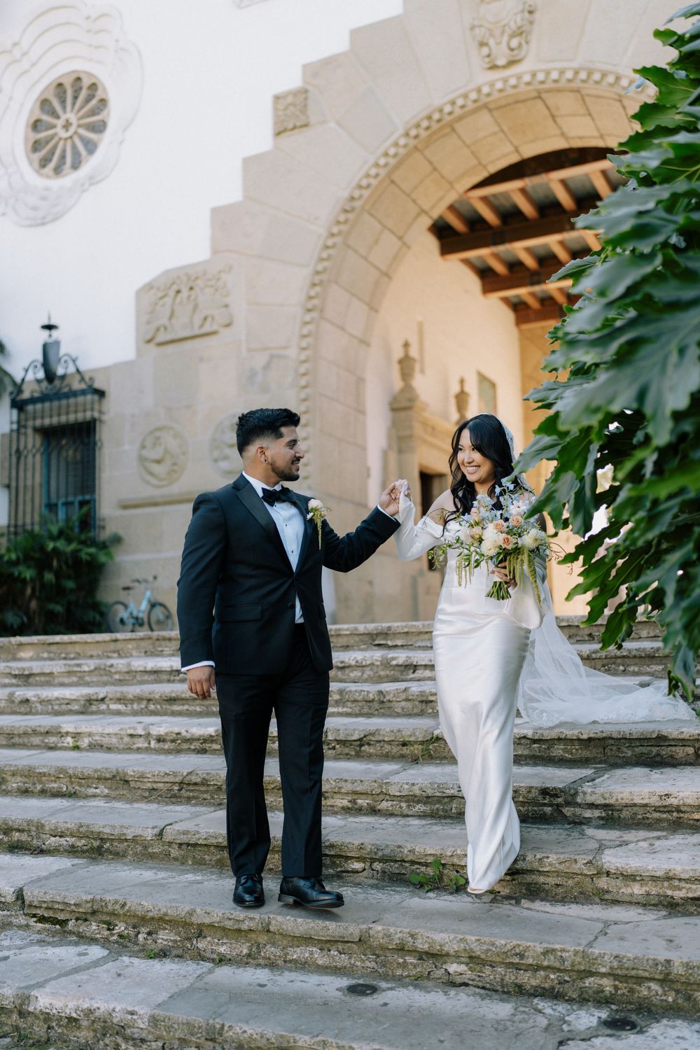 Wedding couple posing on historic stone steps with arched architecture.