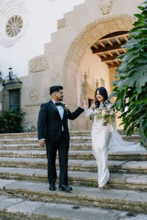 Wedding couple posing on historic stone steps with arched architecture.
