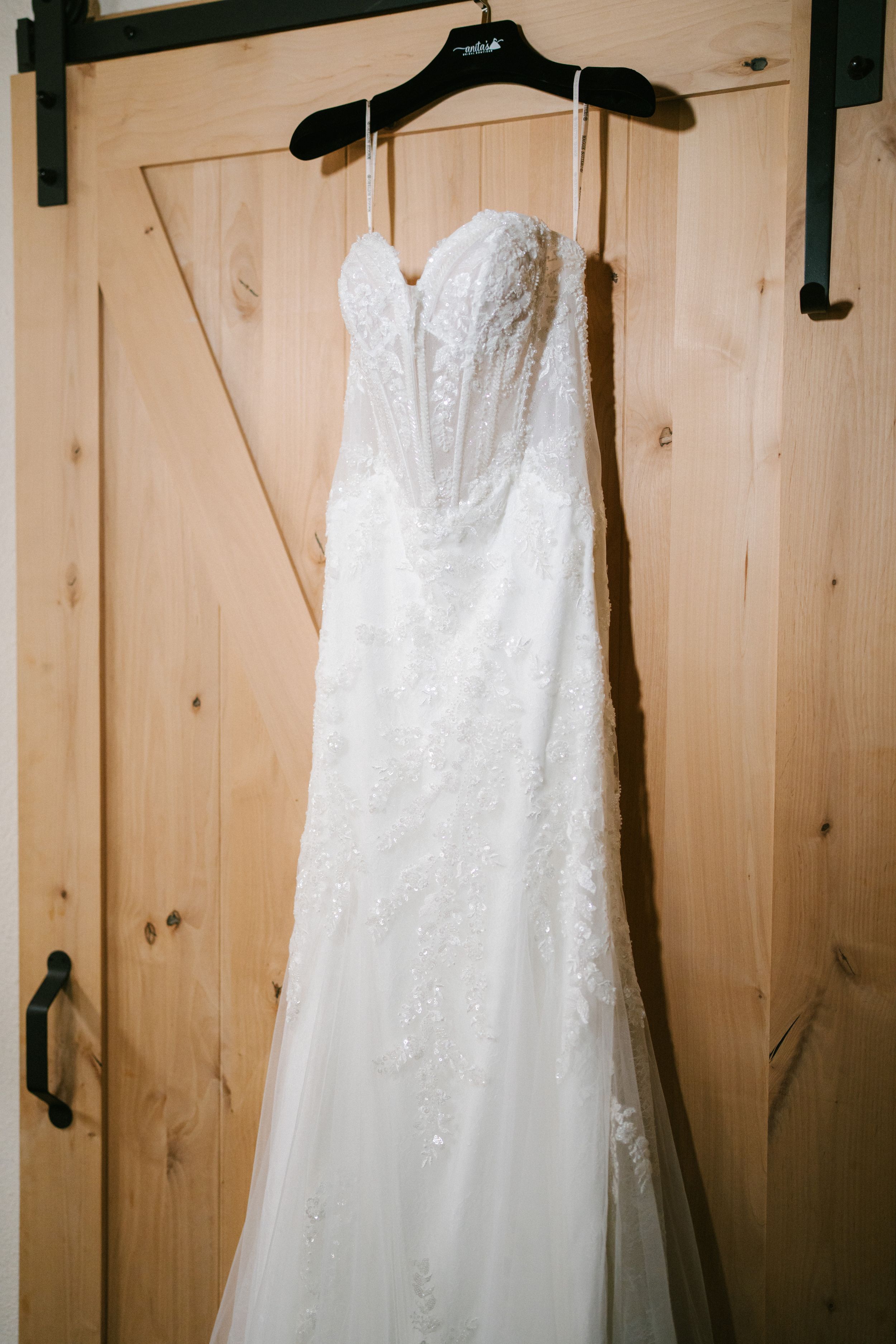 Three elegant white wedding dresses hanging on black hangers against a rustic wooden wall.