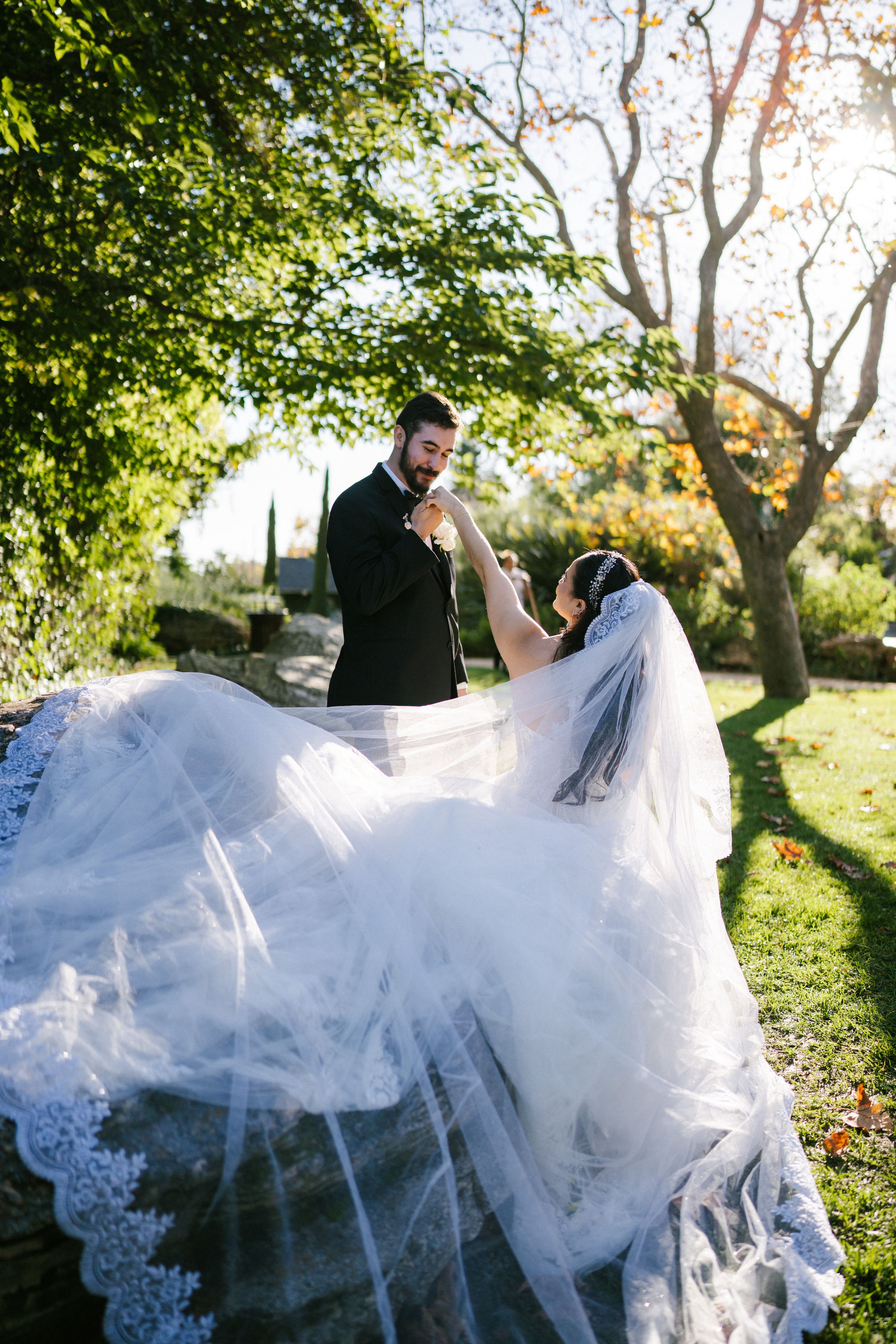 A couple in wedding attire spins playfully in a sunlit garden, creating a flowing movement with the bride's white dress.