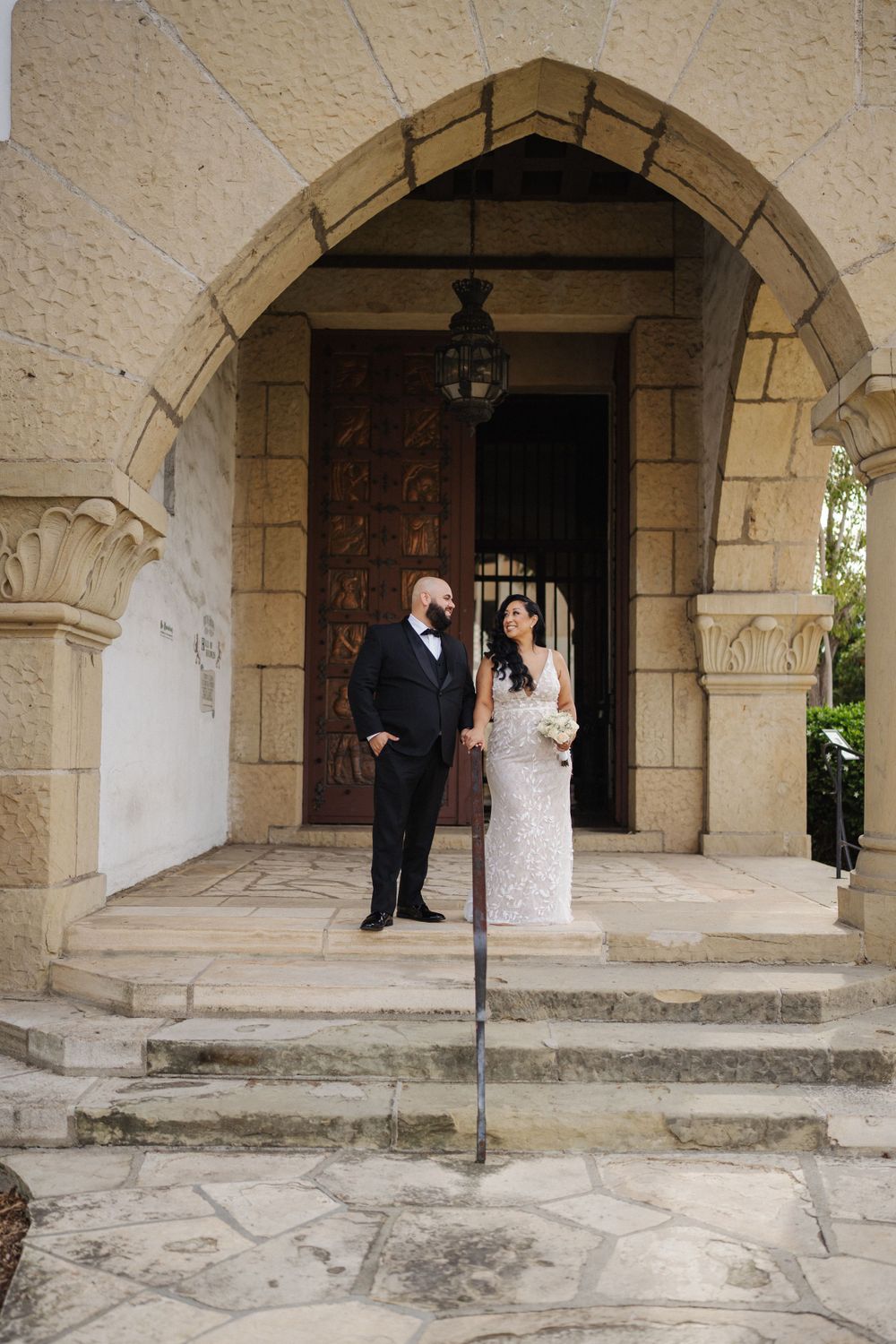 Wedding couple standing in elegant stone archway entrance.