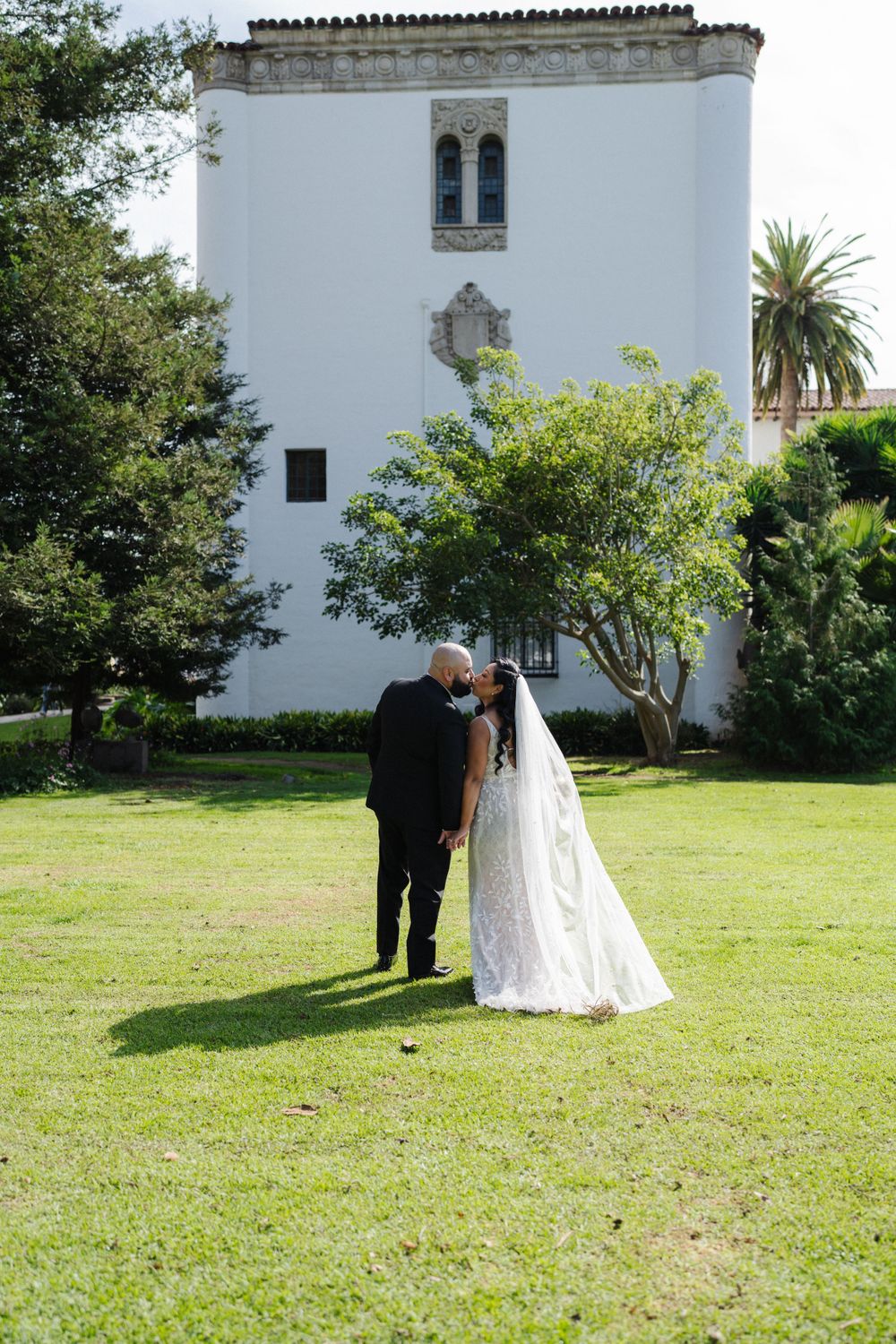Wedding couple walking on lawn near white Mediterranean-style building.