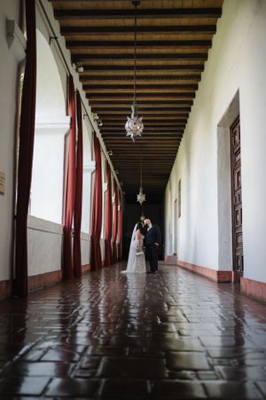 Wedding photo in a historic hallway with exposed wooden beams and red columns.