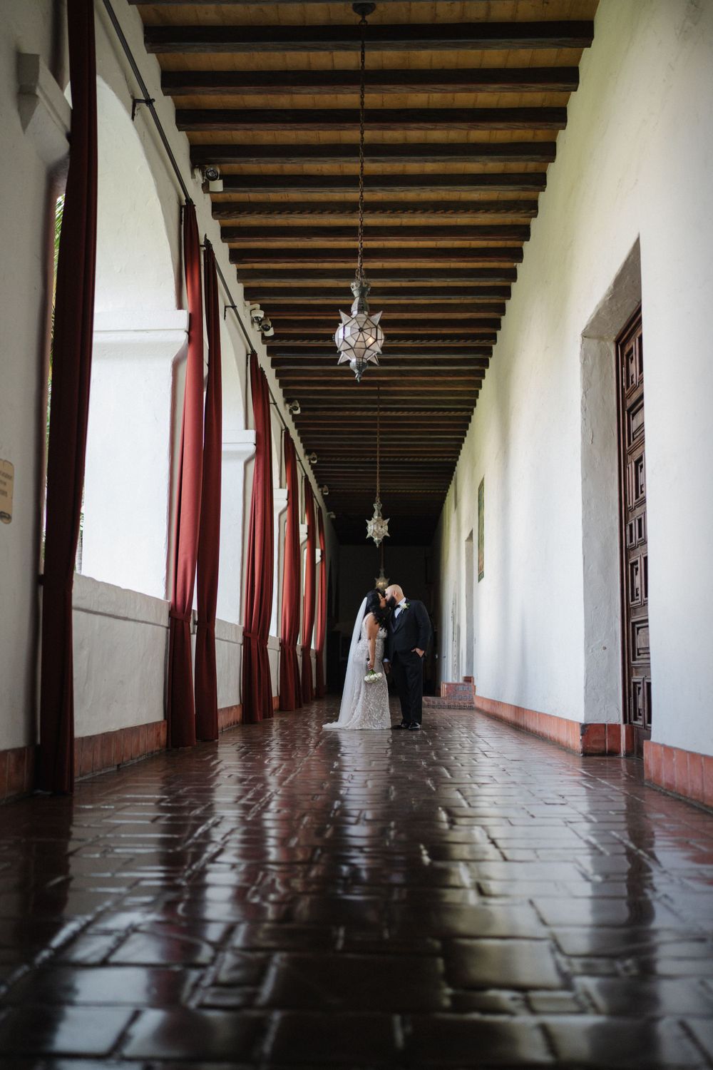 Wedding photo in a historic hallway with exposed wooden beams and red columns.