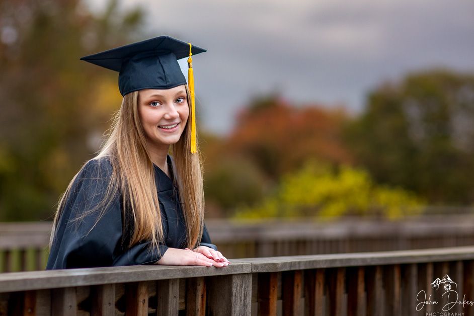 Graduate in black cap and gown smiles during outdoor photo session.