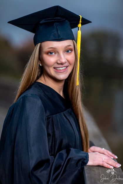 Graduate in black cap and gown poses for outdoor portraits with a yellow tassel.
