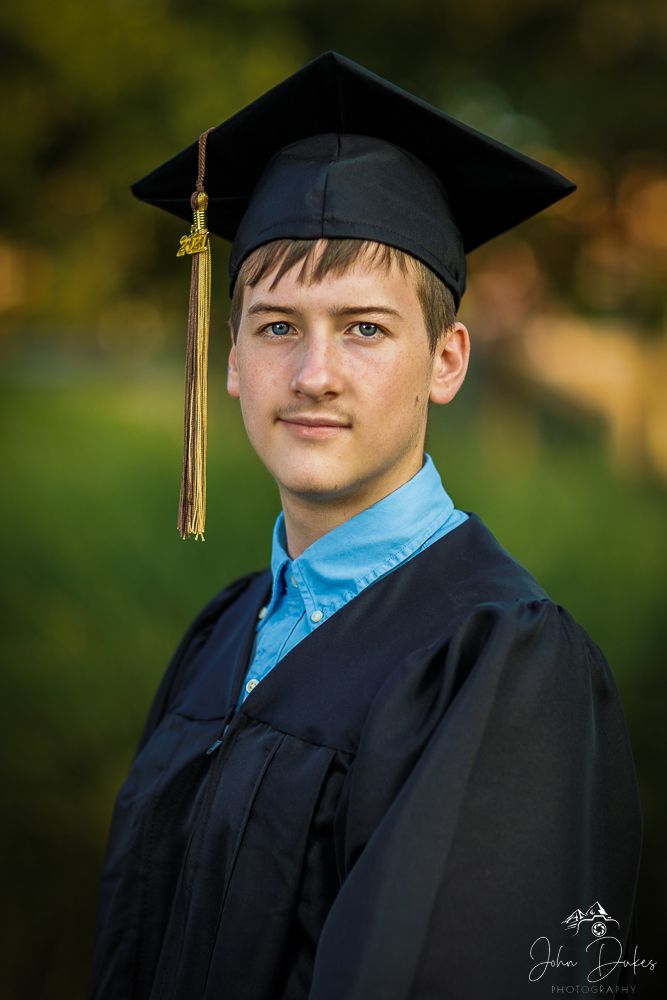 Graduate in black cap and gown with blue shirt poses for portraits outdoors.