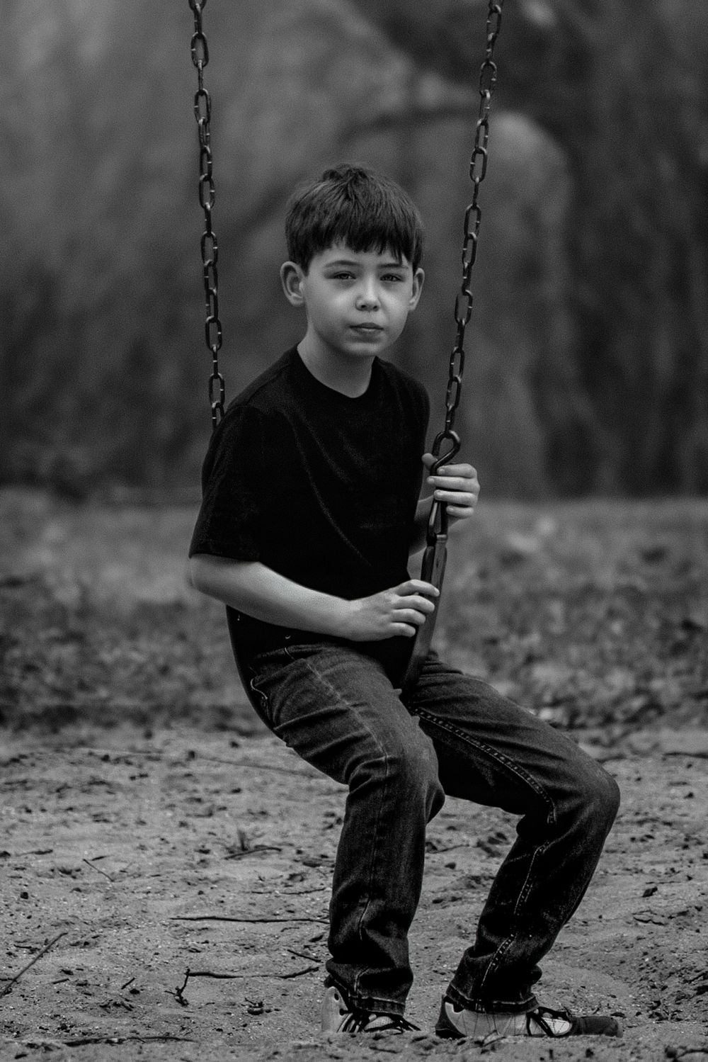 Black and white portrait of a child sitting on a swing in a minimalist setting.