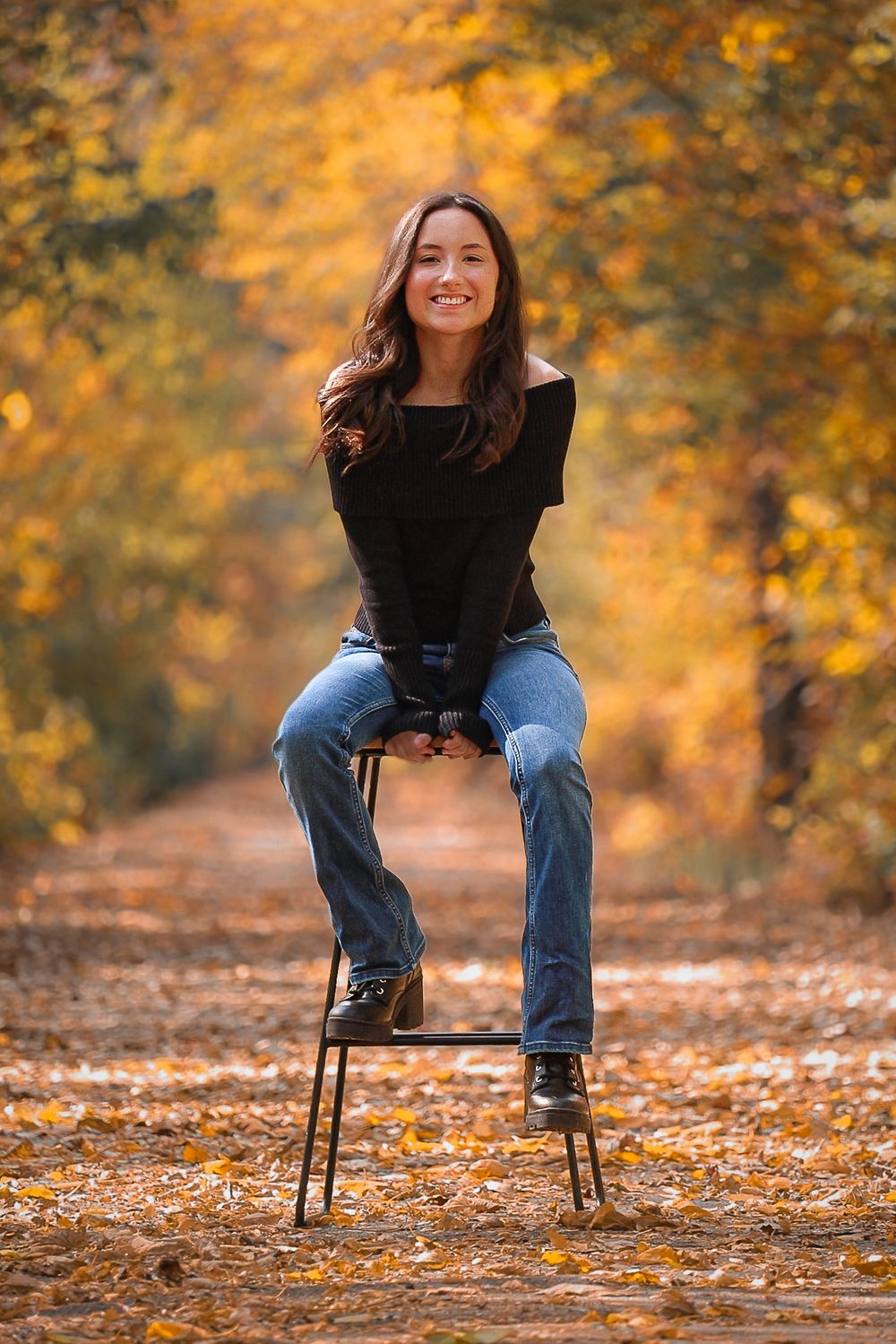 Portrait against autumn foliage background with someone sitting on a stool.