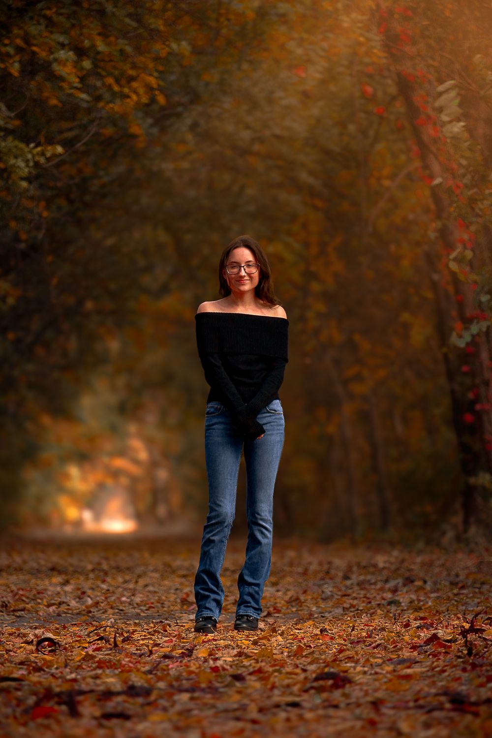 Portrait in autumn forest with person wearing black off-shoulder top and jeans.