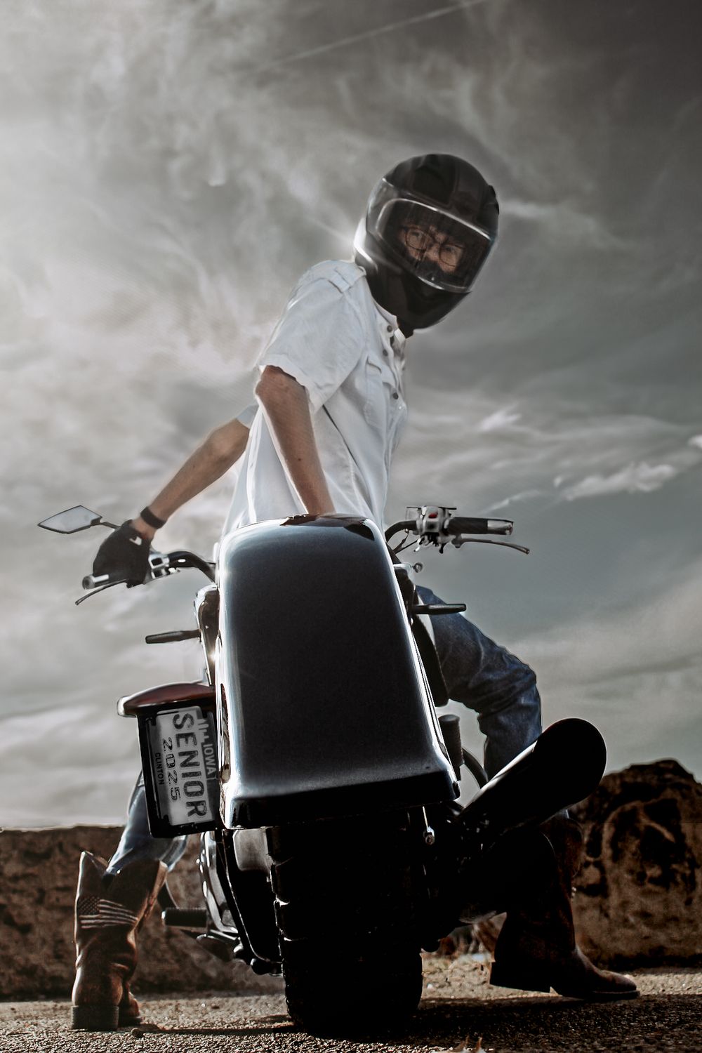 Dramatic shot of a motorcyclist in white shirt and helmet against stormy sky.