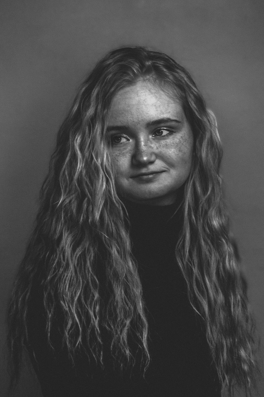 Black and white portrait of someone with long wavy hair and freckles.