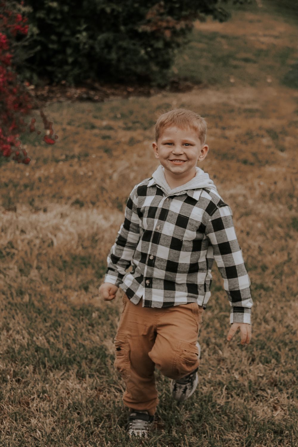 Child in buffalo plaid shirt and brown pants plays on autumn grass.