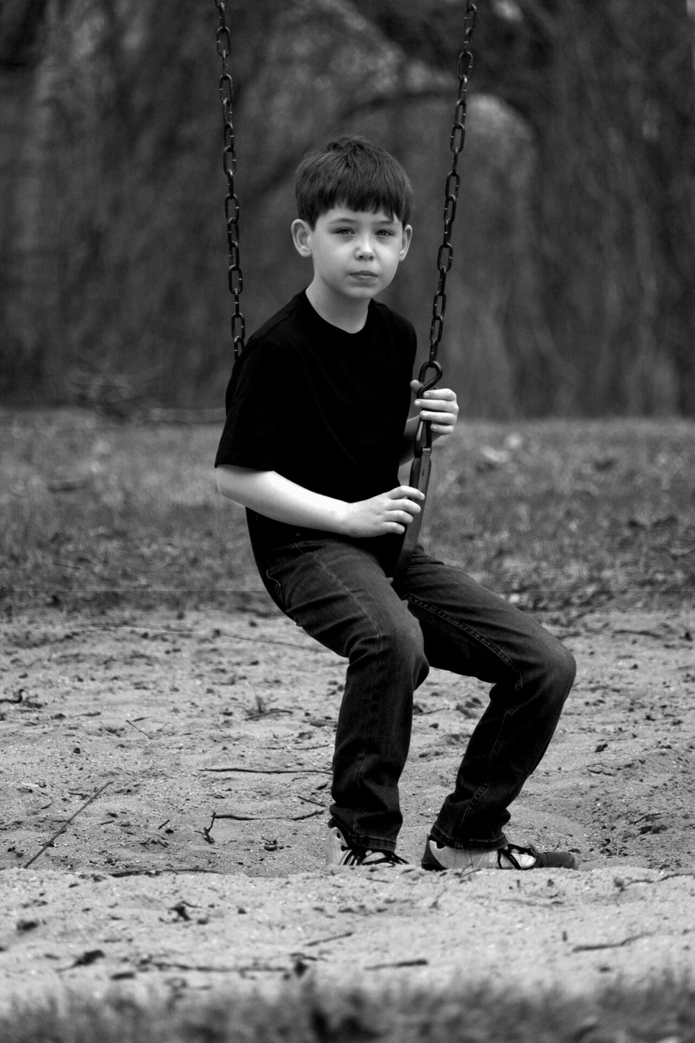 Black and white photo of someone sitting on a playground swing in casual attire.