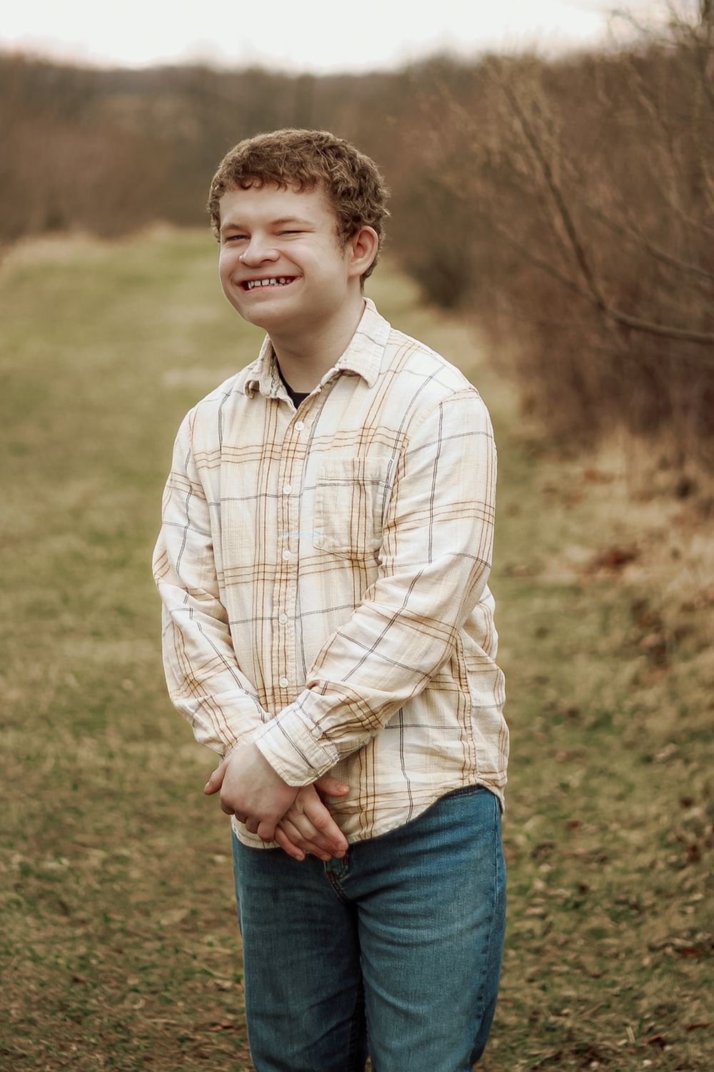 Portrait of someone in a plaid shirt smiling outdoors against a natural backdrop.