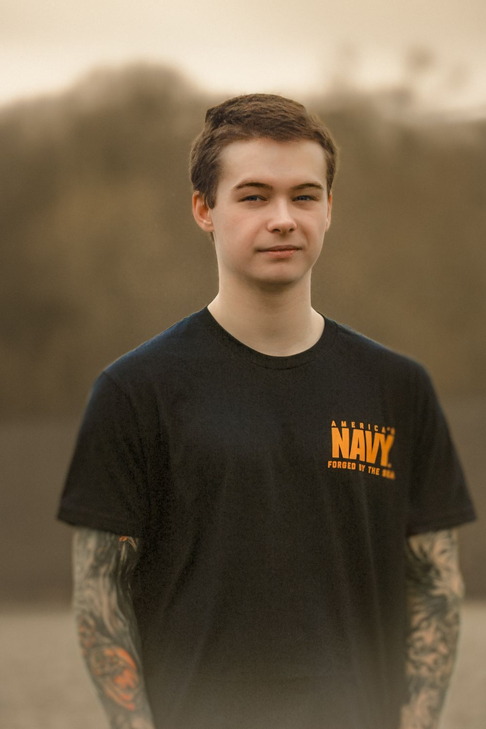 Portrait of someone wearing a black Navy t-shirt with visible arm tattoos.