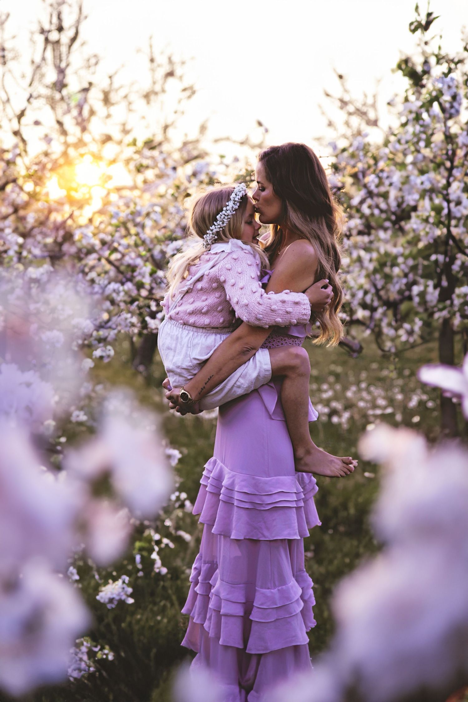 Dreamy spring portrait in a flowering orchard with flowing lavender dress at sunset.