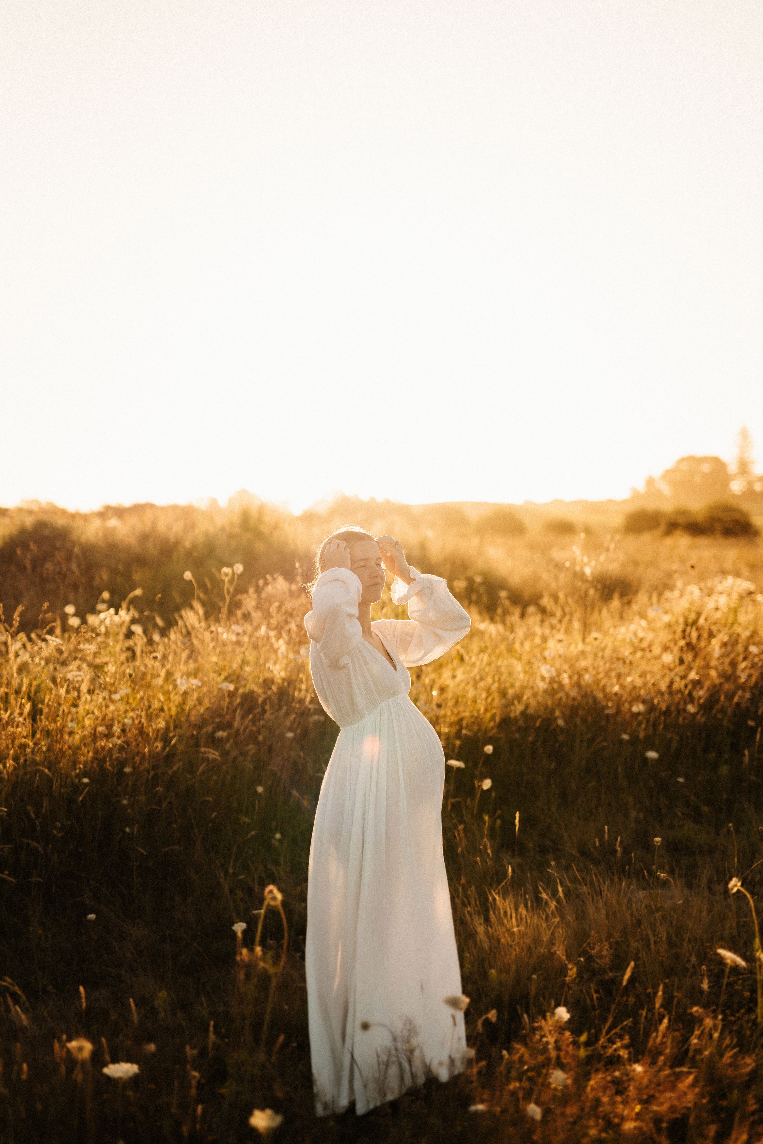 Dreamy white dress maternity silhouettes in a golden sunset field.