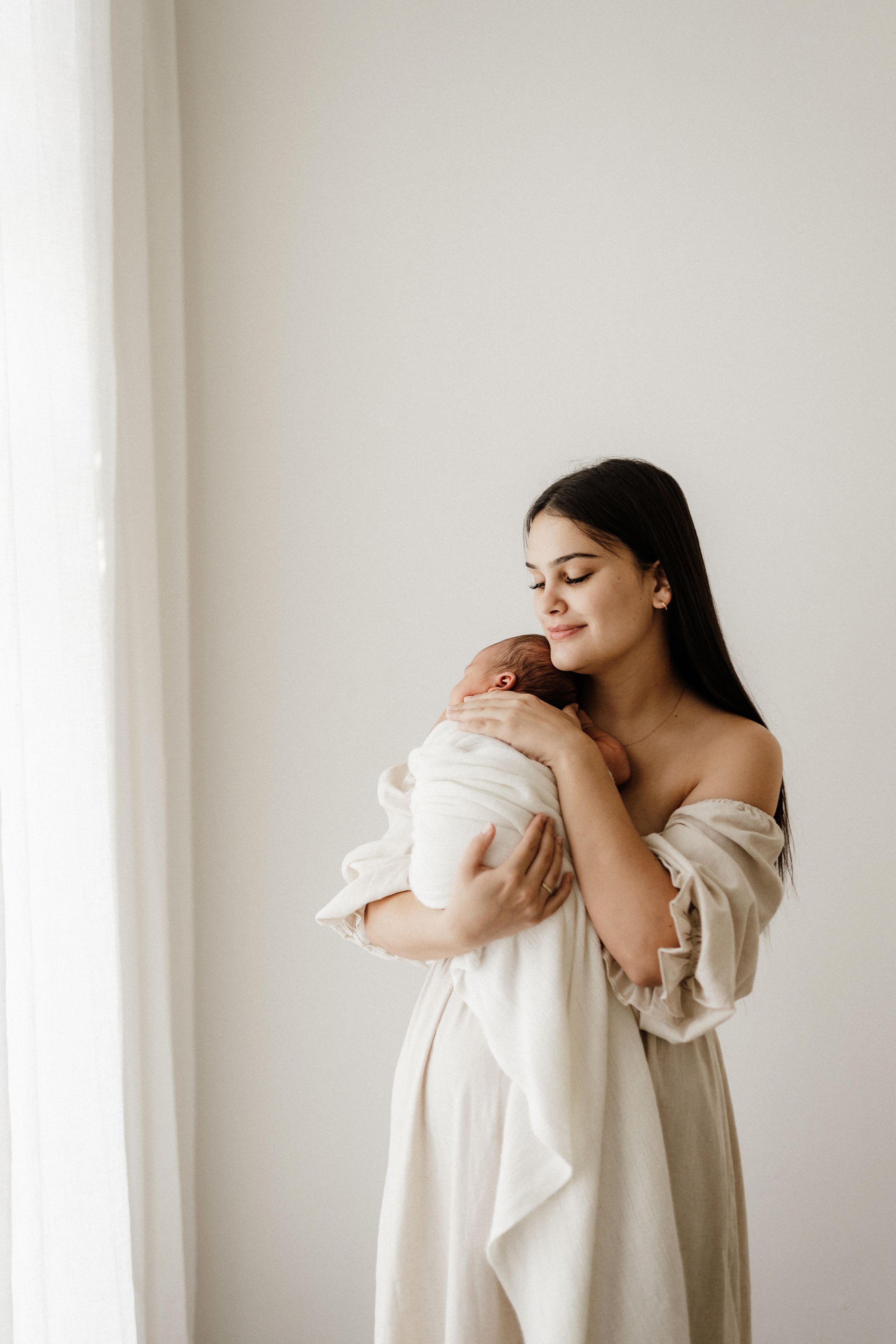 Soft emotional motherhood portraits against clean white backdrop in natural light.
