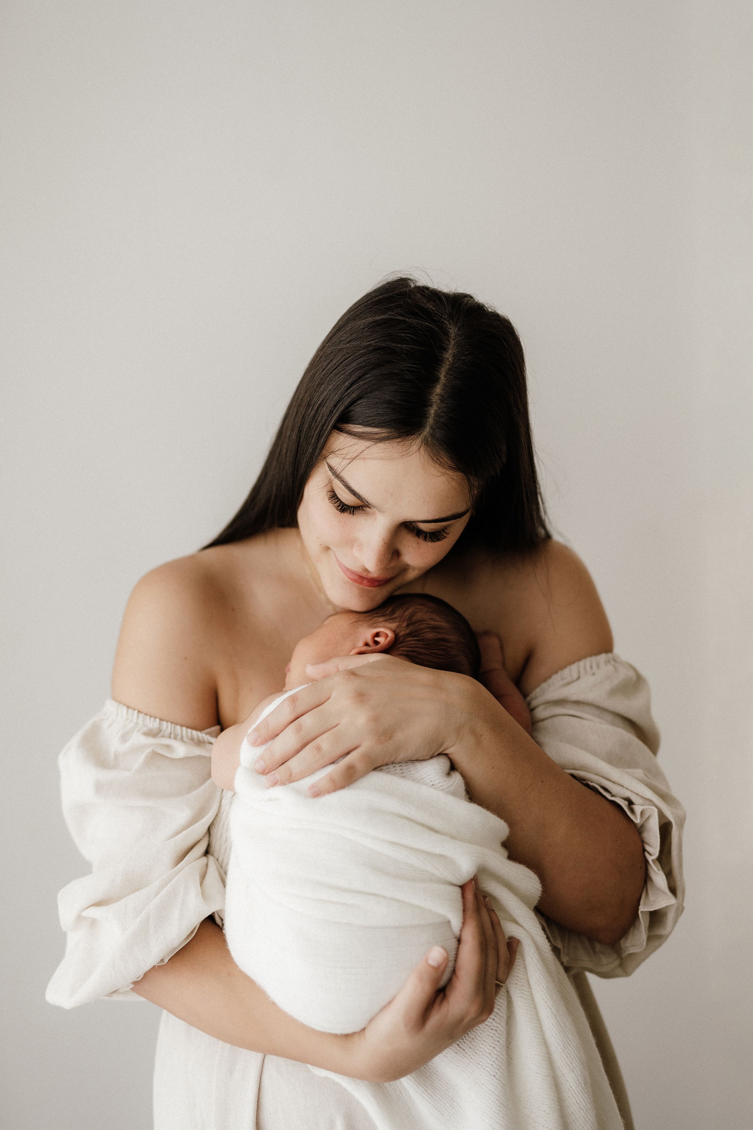 Intimate motherhood series in white featuring tender moments against neutral backdrop.