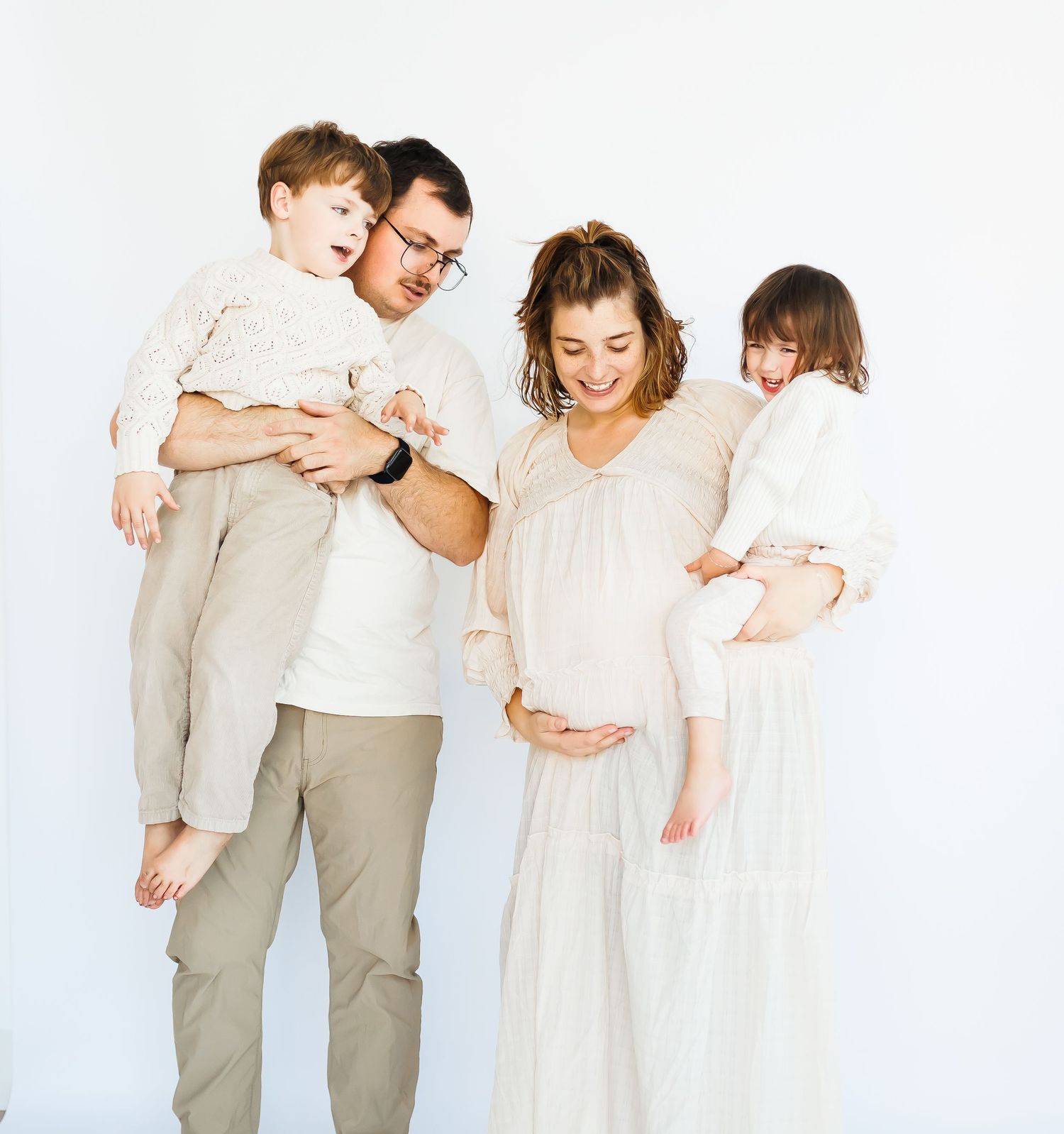 A family wearing white and beige outfits poses together against a light background.