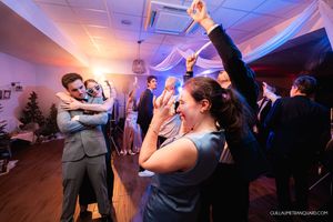 Wedding guests dancing enthusiastically under colorful lighting at an indoor reception.