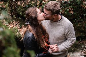 Romantic couple embraces in a lush forest setting during an autumn engagement photoshoot.