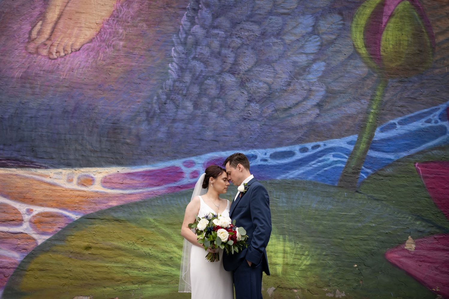 A tender wedding moment between newlyweds surrounded by autumn foliage with a white floral bouquet.