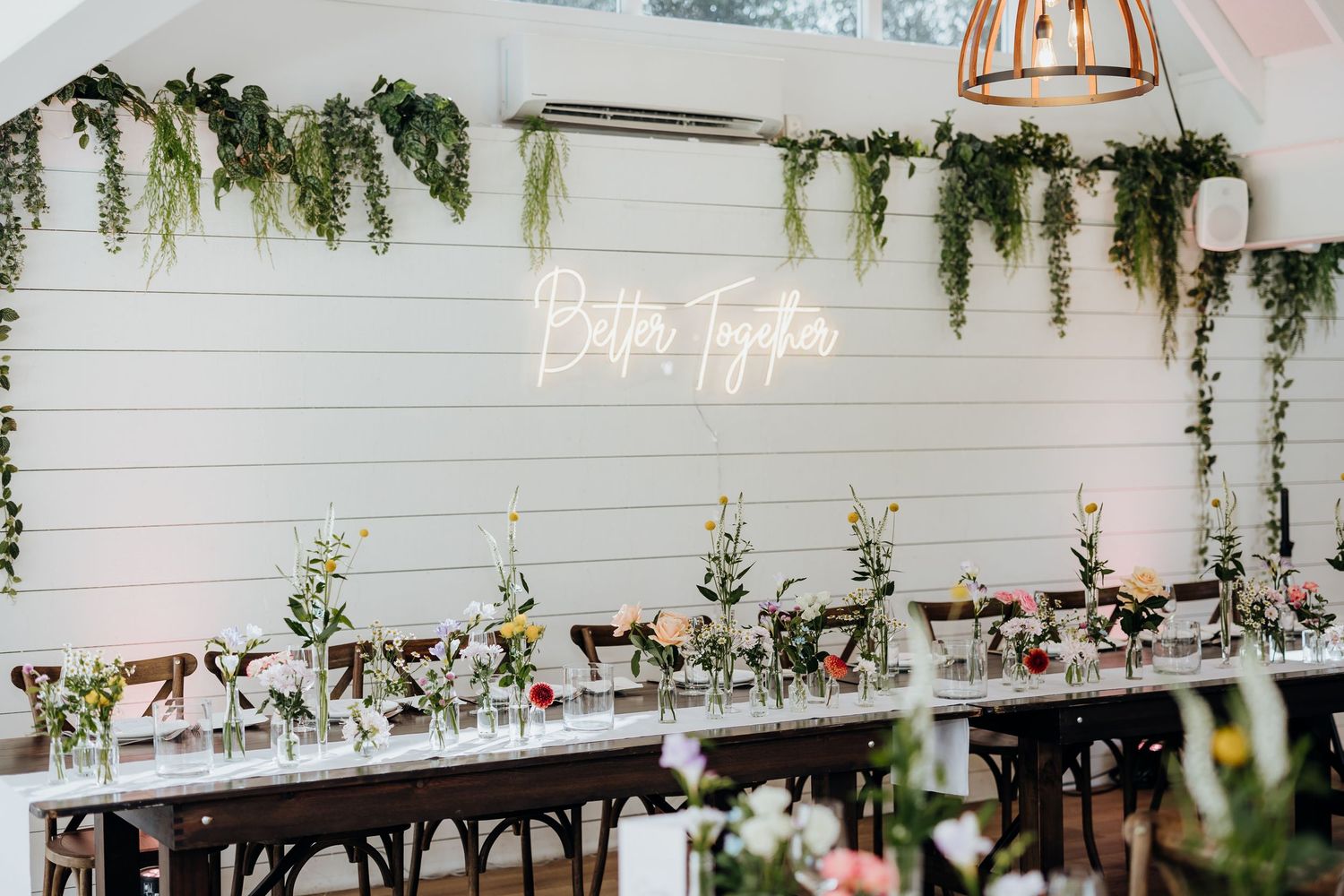 Wedding reception venue with rustic wooden table settings and elegant hanging greenery in an industrial-style space.