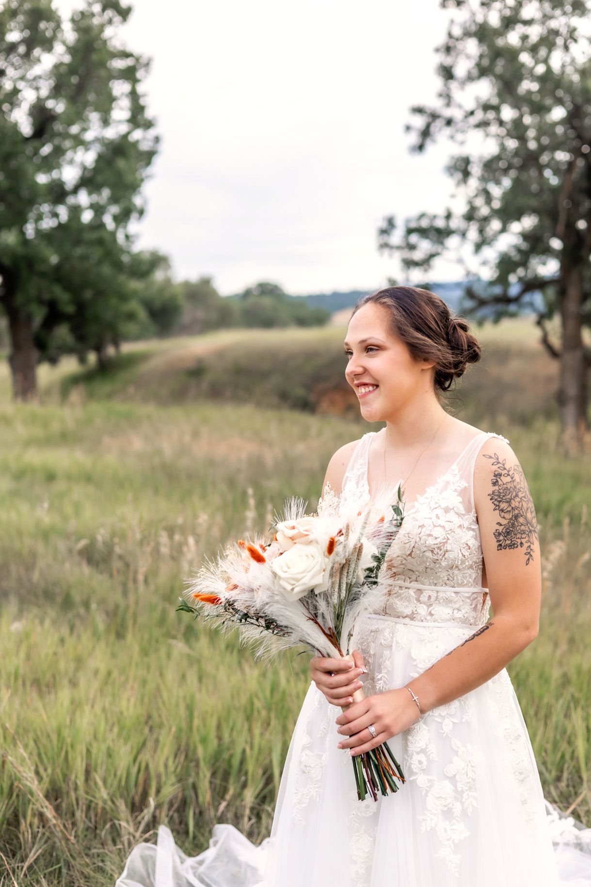 Bride in flowing white gown poses elegantly in vintage chair by floral artwork.