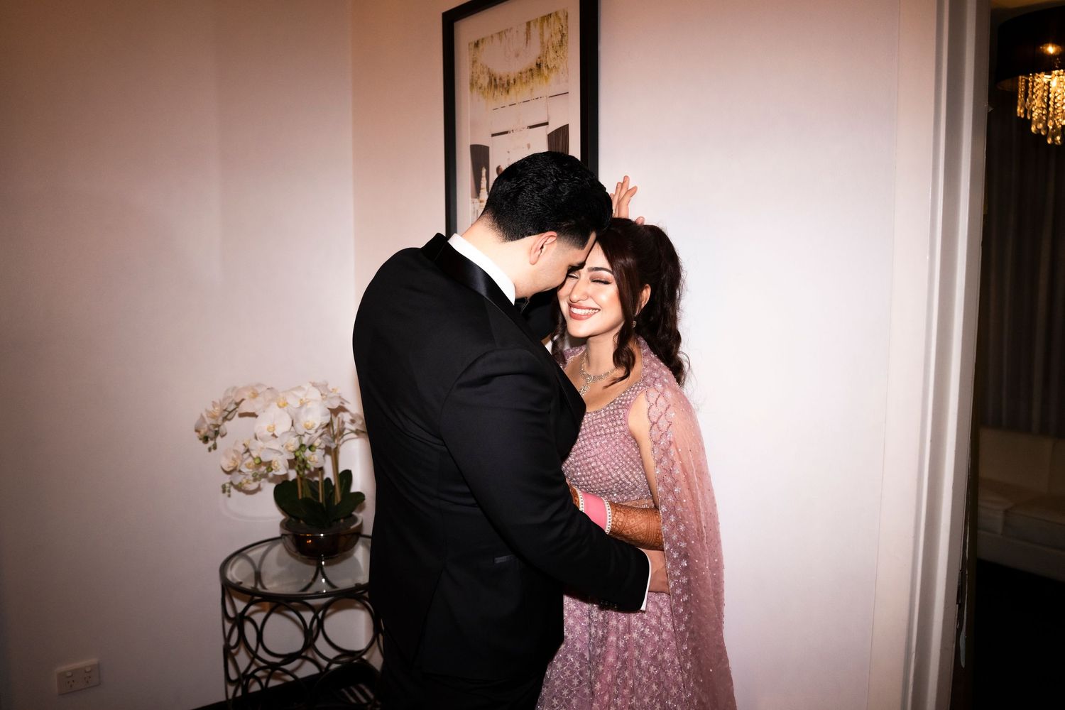 A couple share an intimate moment together, with one wearing a black suit and the other in a pink dress.