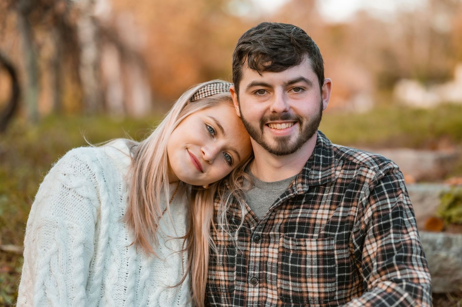A couple shares a joyful moment embracing outdoors during autumn with golden bokeh in the background.