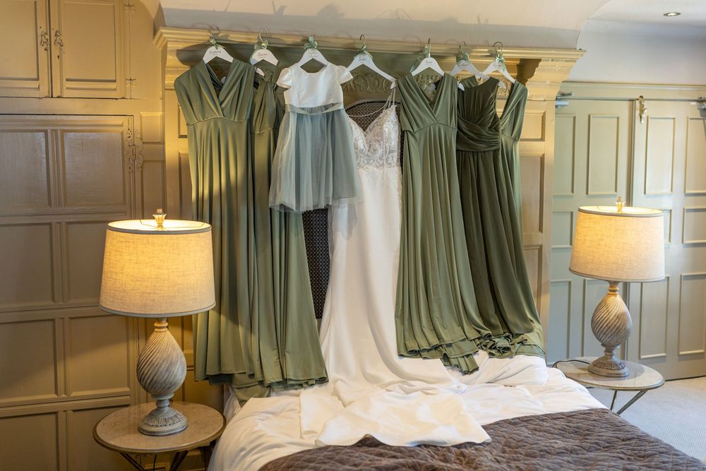 White wedding gown and sage green bridesmaid dresses hanging on a wardrobe in a elegant bridal suite.